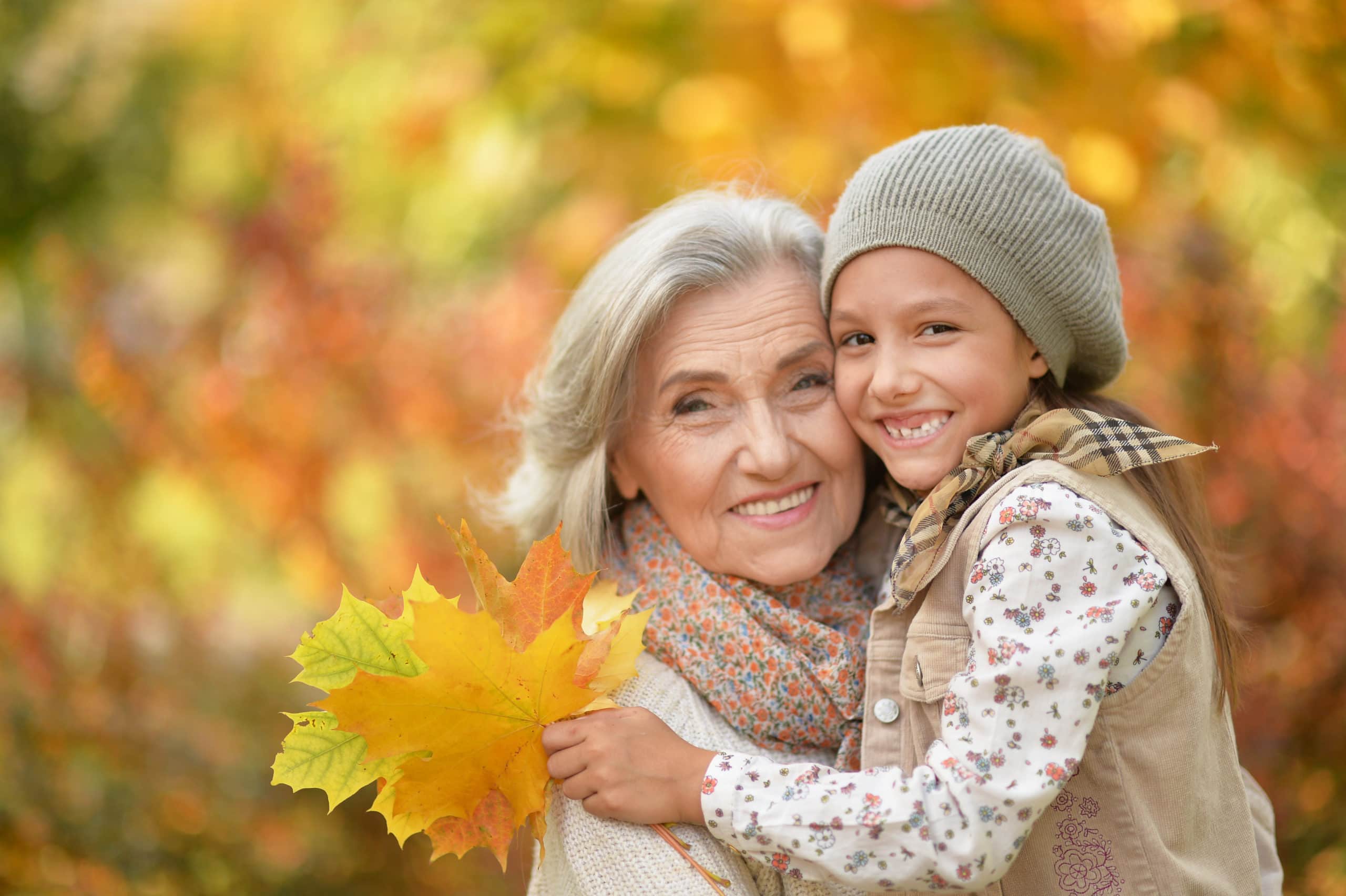 grandmother with granddaughter smiling holding autumn leaves