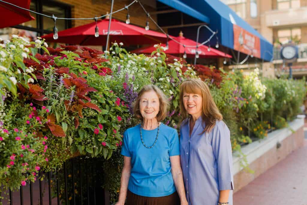 Two women standing in front of a restaurant with flowers.