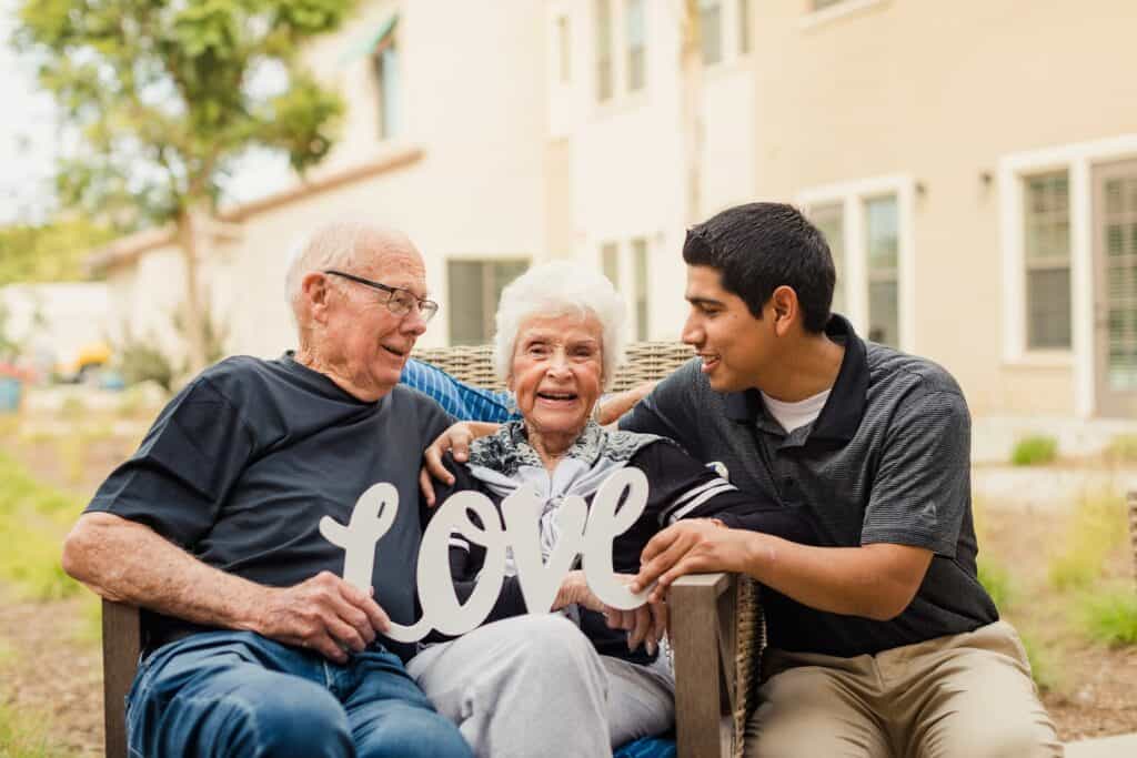 An elderly couple sitting on a bench with a sign that says love.