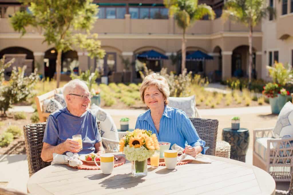 An elderly couple enjoying breakfast outside at a retirement community.