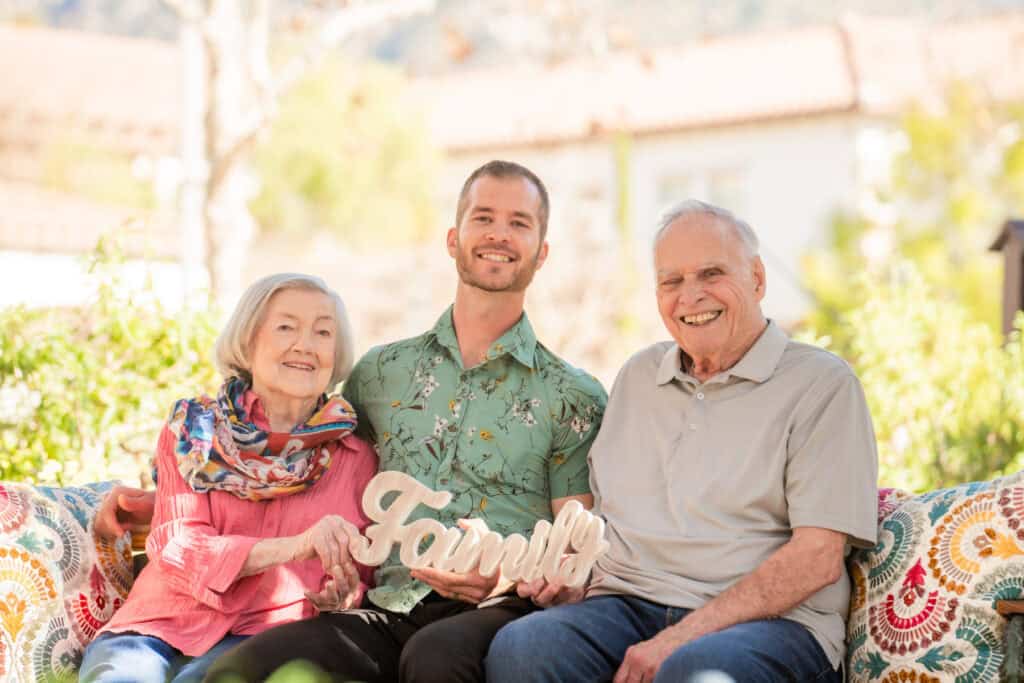 young man sitting with older couple holding sign that says family